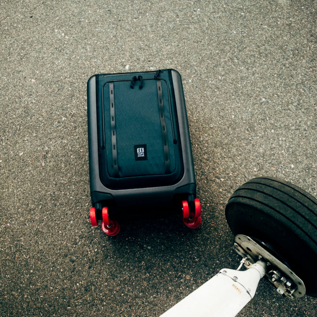 A black suitcase with red wheels next to an airplane tire.