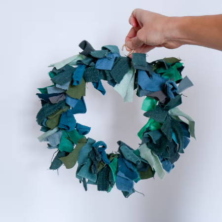 hand holding a finished wreath made out of green fabric scraps