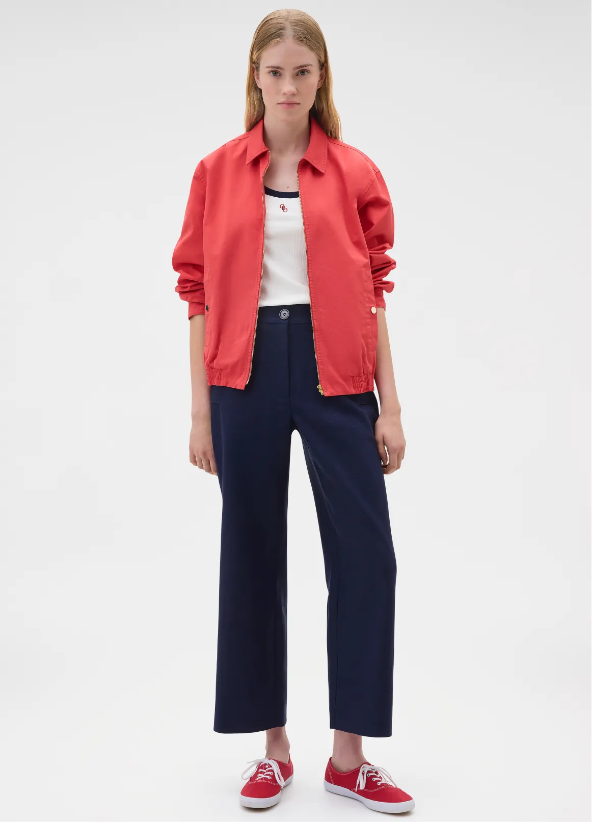 Model wearing a red jacket, white top, and navy pants with red shoes.