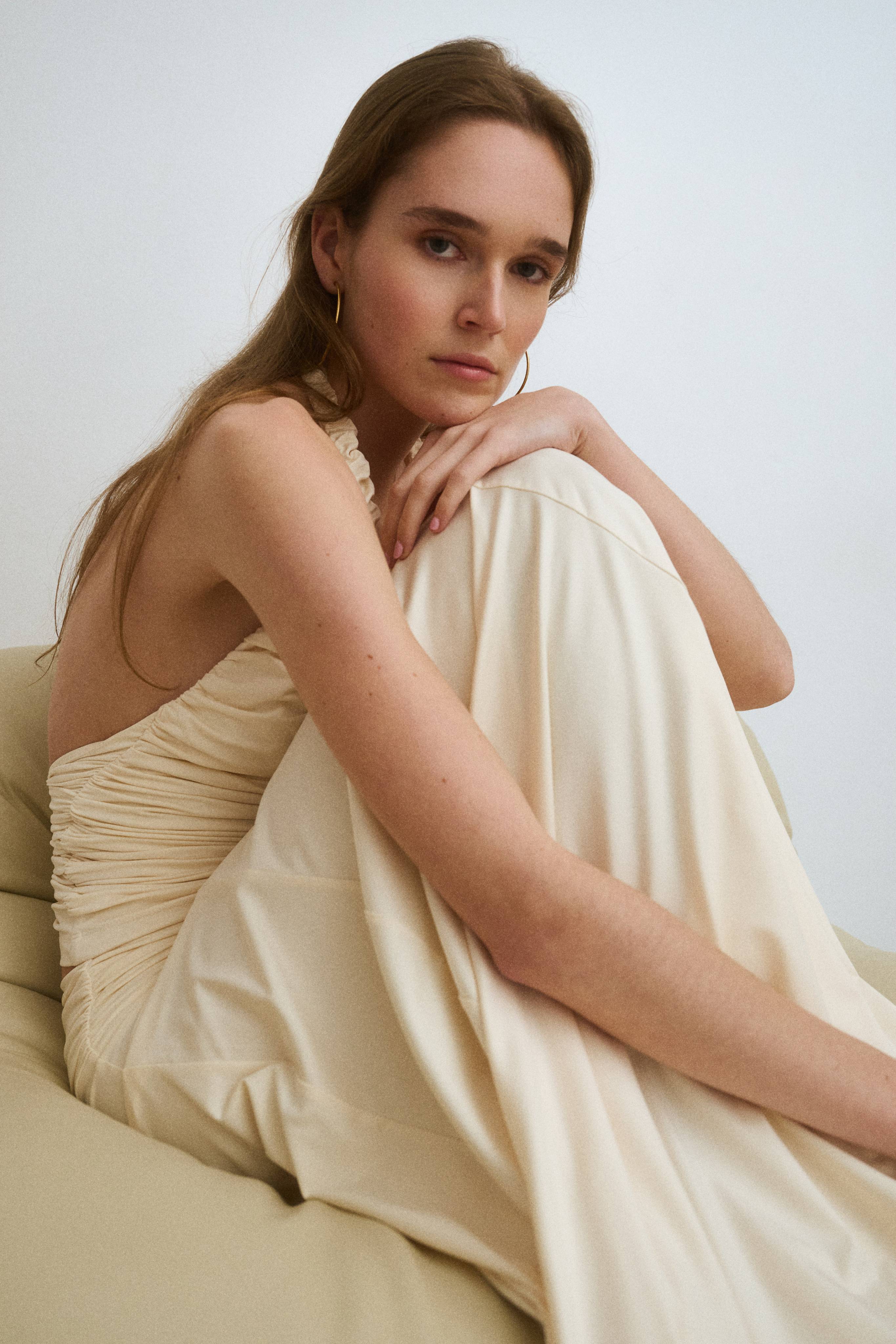 A person sitting on a couch, wearing a flowing cream-colored dress.