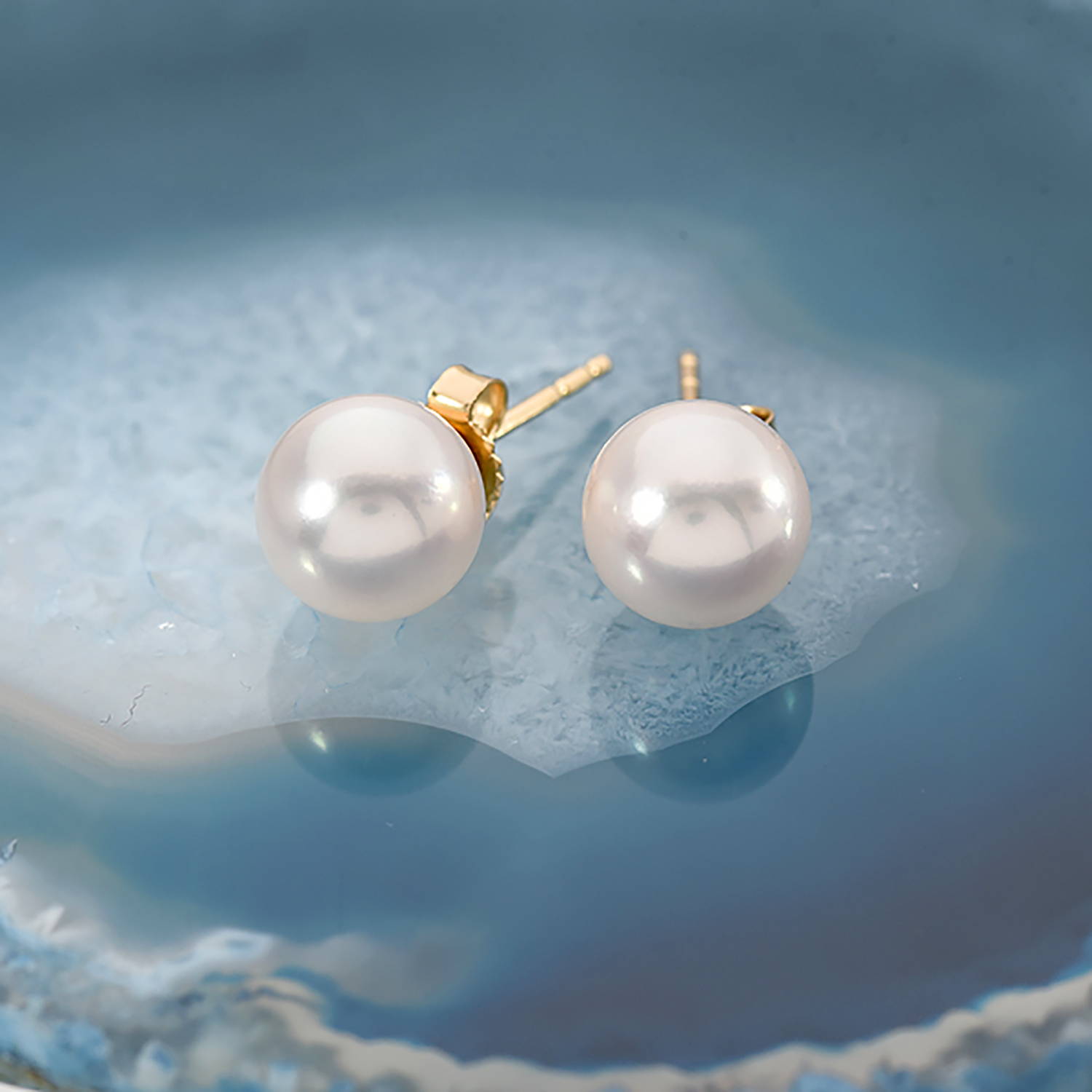 A pair of white Akoya pearl earrings on a blue geode slice