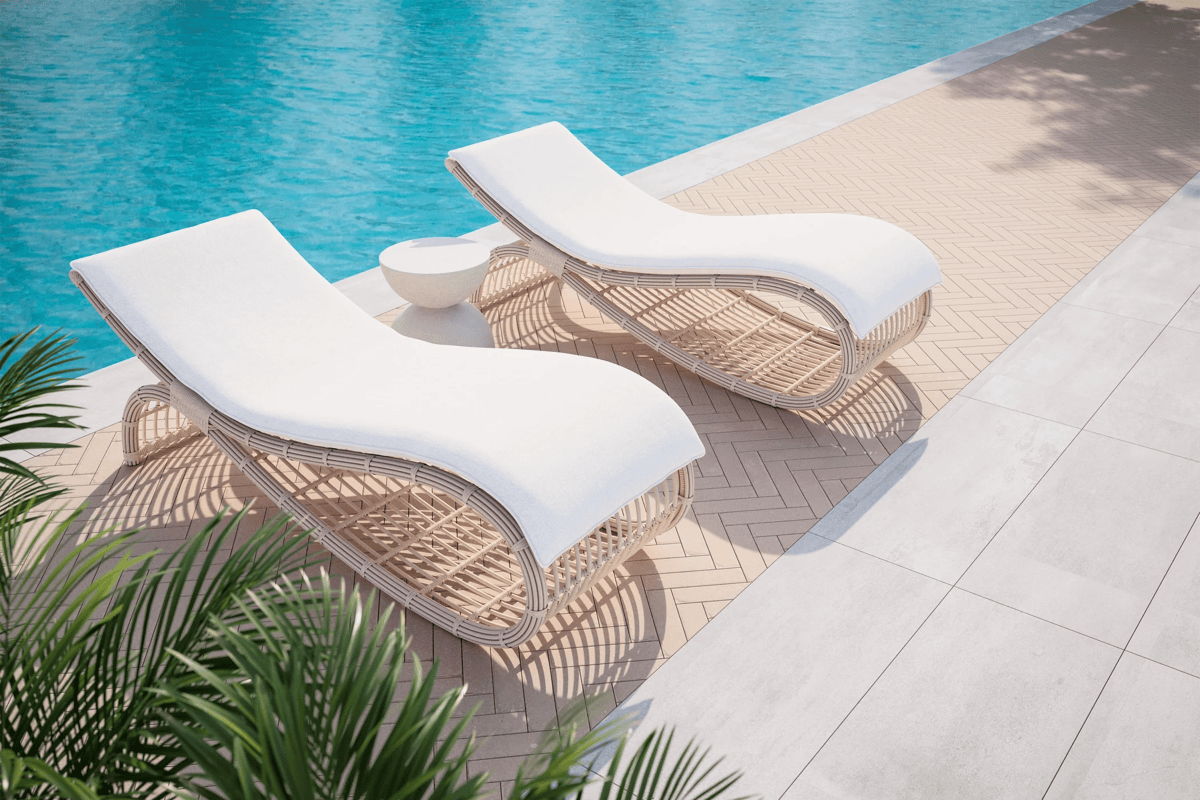 Two curved white-cushion pool loungers on a herringbone patio next to a bright blue swimming pool.