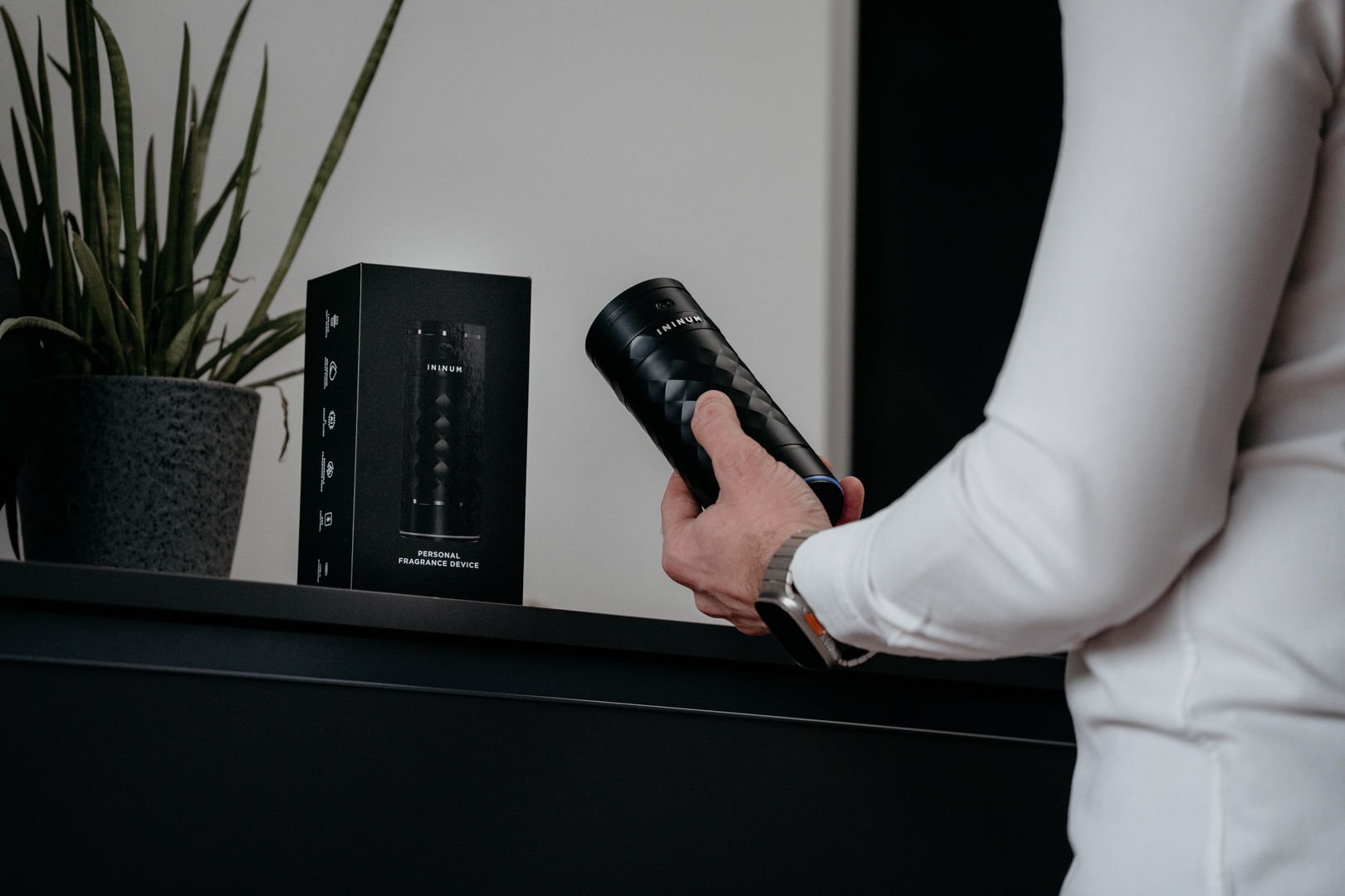 Person holding a black cylindrical object near a speaker and plant.