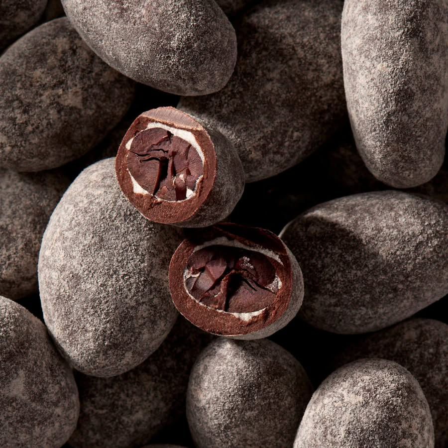 Chocolate-covered coffee beans on a textured surface, some cut open.