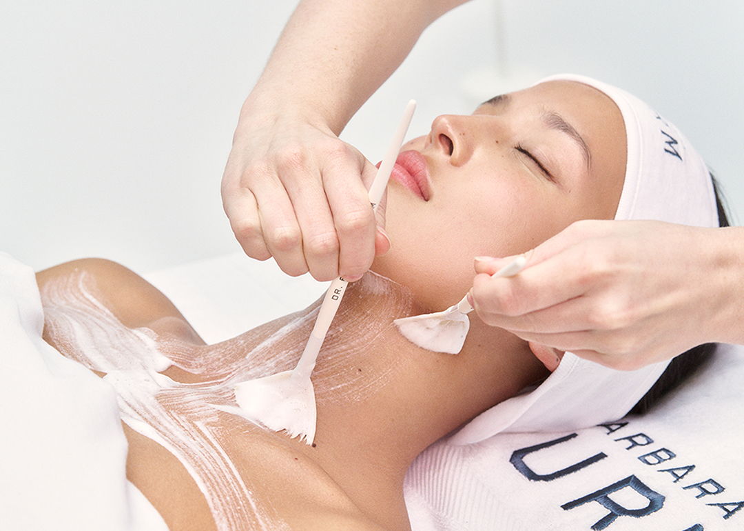 Woman receiving facial treatment with hands applying a mask.