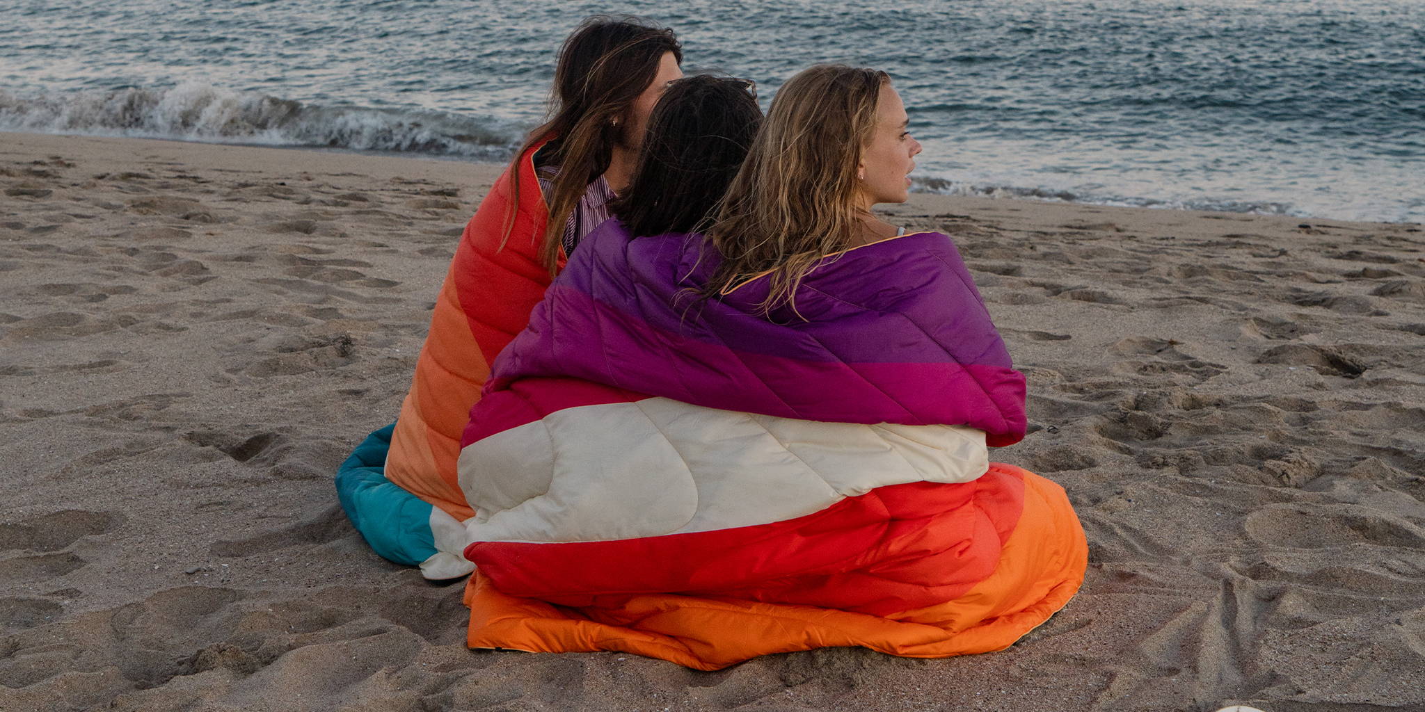 Three Women Sitting on Beach Wrapped In Original Puffy Blankets