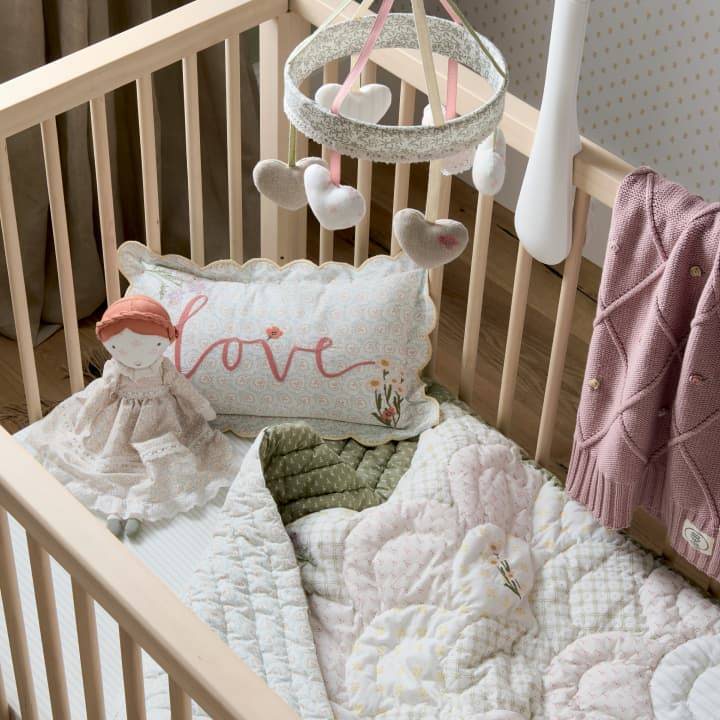 A wooden cotbed has a Laura Ashley floral cot mobile, blanket and pillow creating a cosy sleep space.