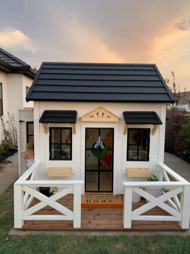 Modern farmhouse style Custom Playhouse with safety glass door, black metal roof and wooden porch by WholeWoodPlayhouses