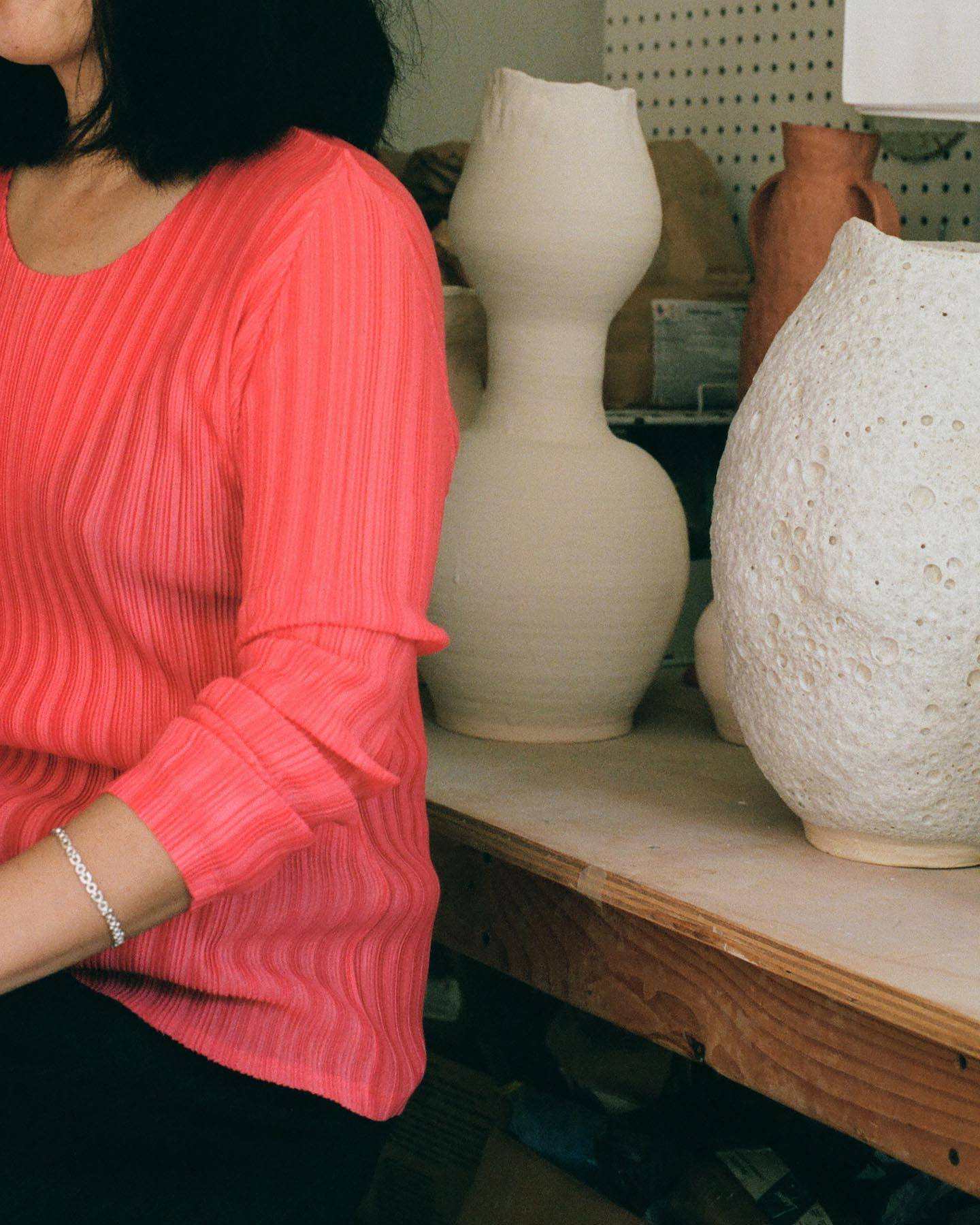 Raina Lee in her studio in a red pleats please shirt and silver chain bracelet.