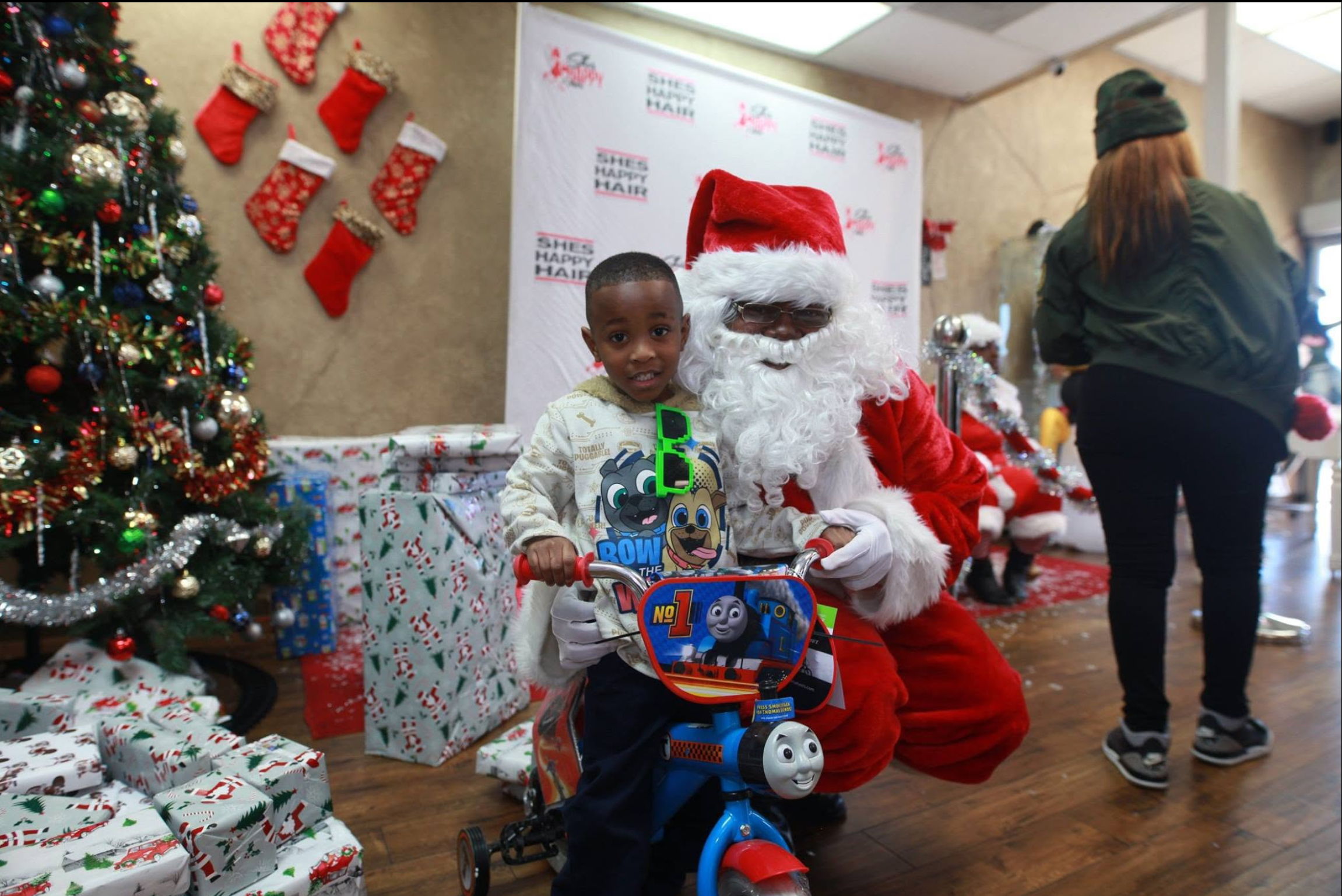Child on bicycle with Santa in holiday-themed setting. She's Happy Hair