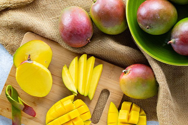 Sliced mangoes on a cutting board with whole mangoes in a bowl.