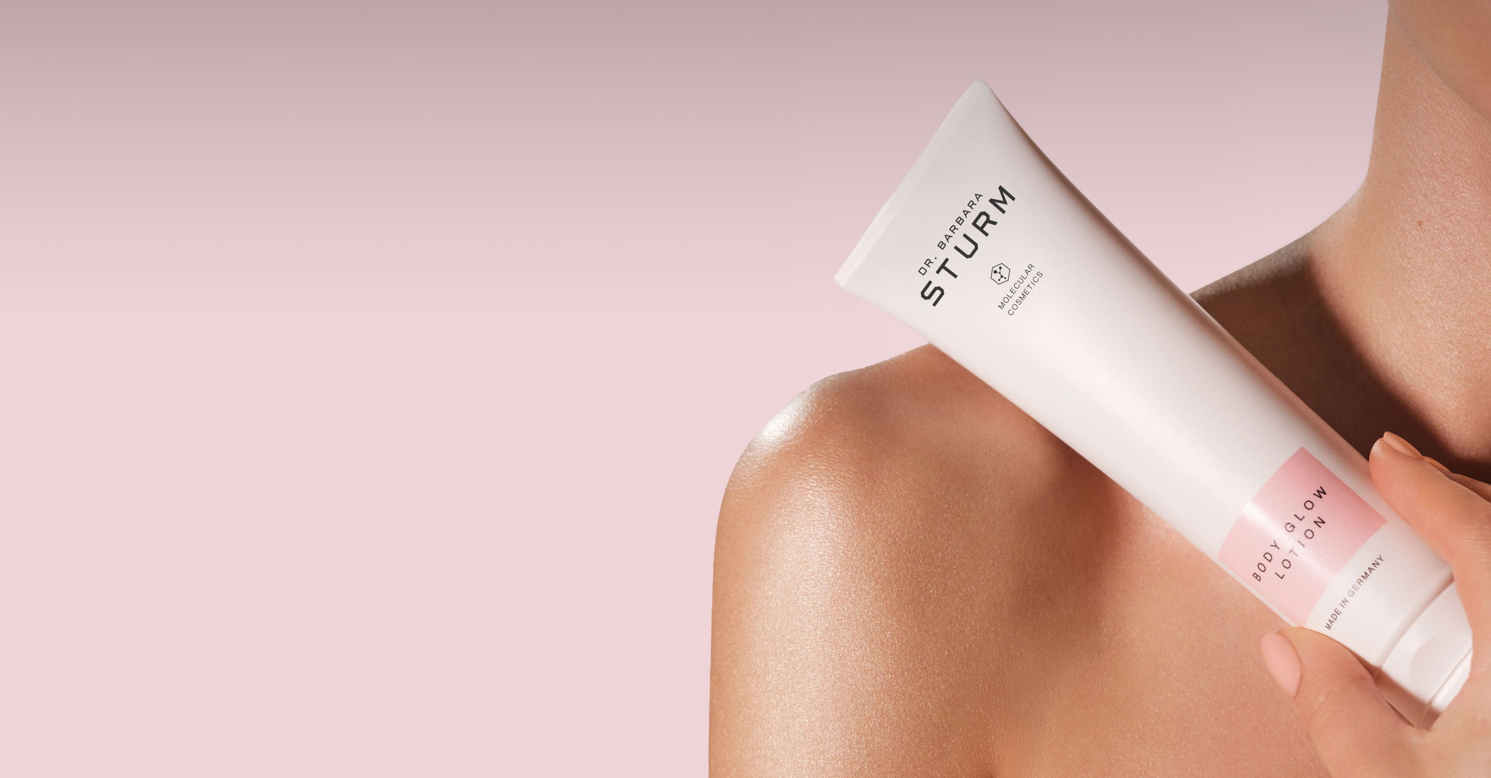 A person holding a tube of skincare product against a pink background.