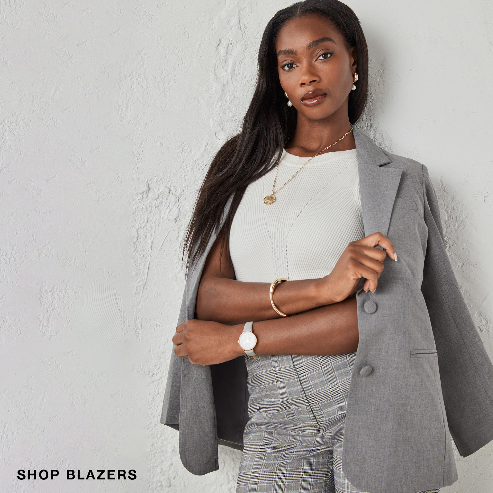 A woman in a gray blazer poses against a light wall.