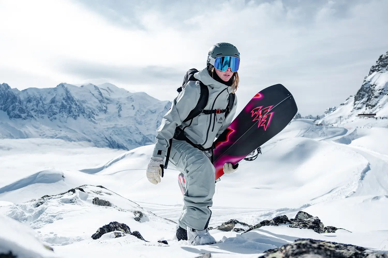 Snowboarder in snowy landscape, holding a snowboard, wearing winter gear.