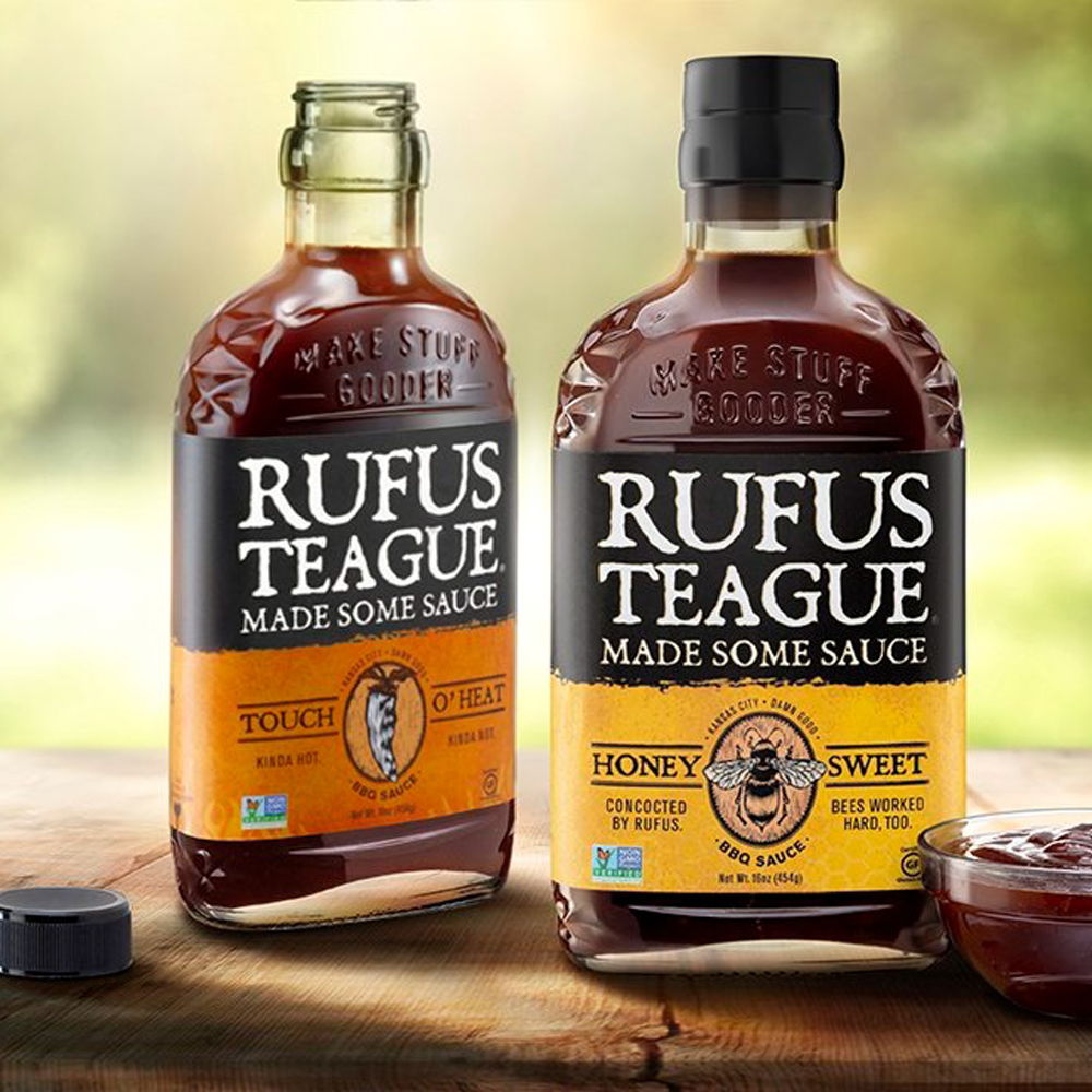 Two bottles of Rufus Teague barbecue sauce on a wooden table.