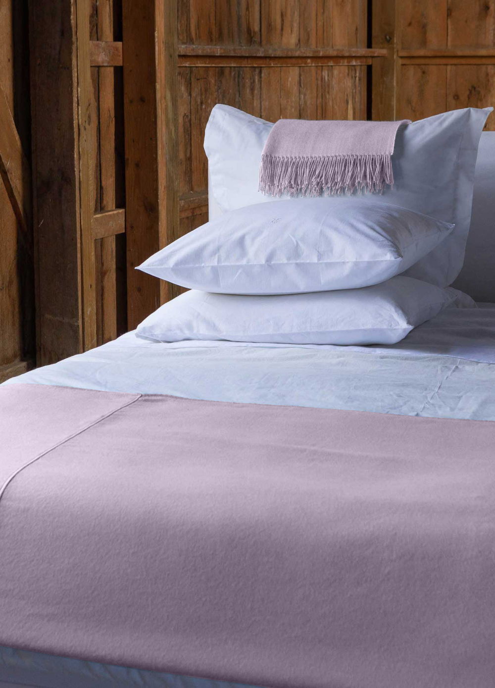 Bedding with white pillows and a pink throw on a wooden bed frame.