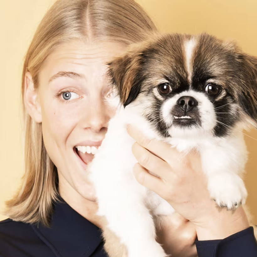 Eine junge Frau, die einen kleinen Hund im Arm hält und vielleicht eine allergische Bindehautentzündung hat.