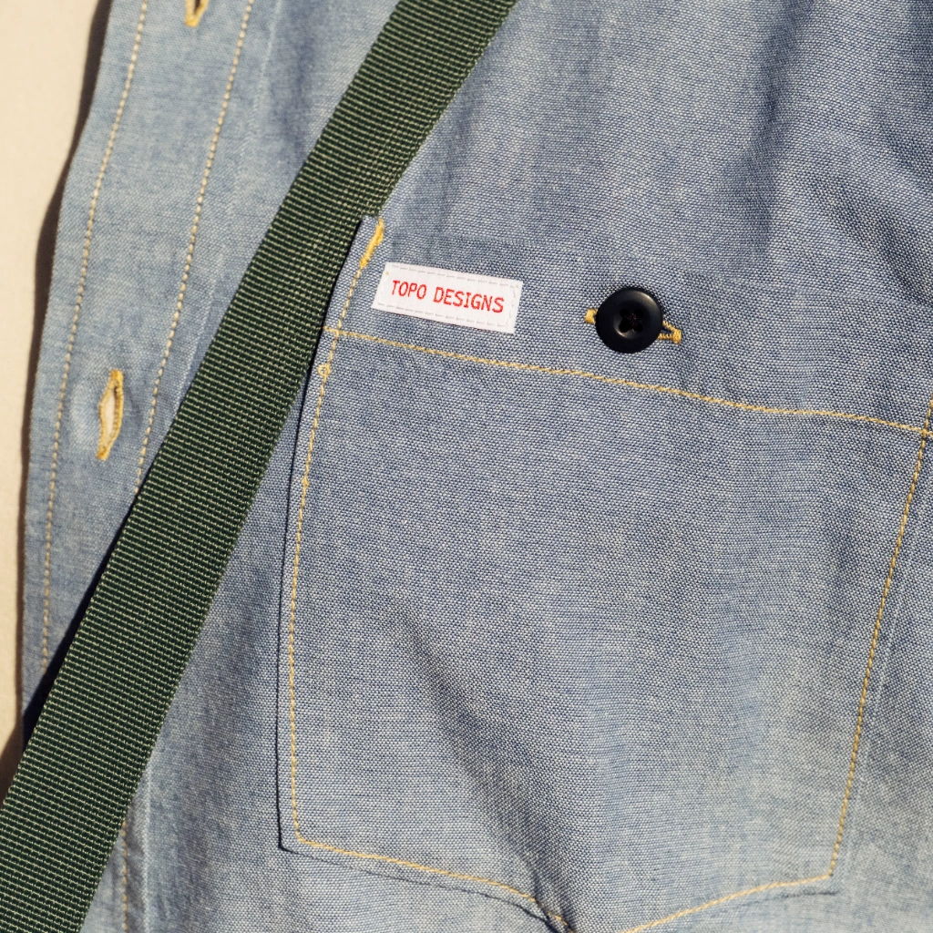 Denim shirt with a pocket and green strap.