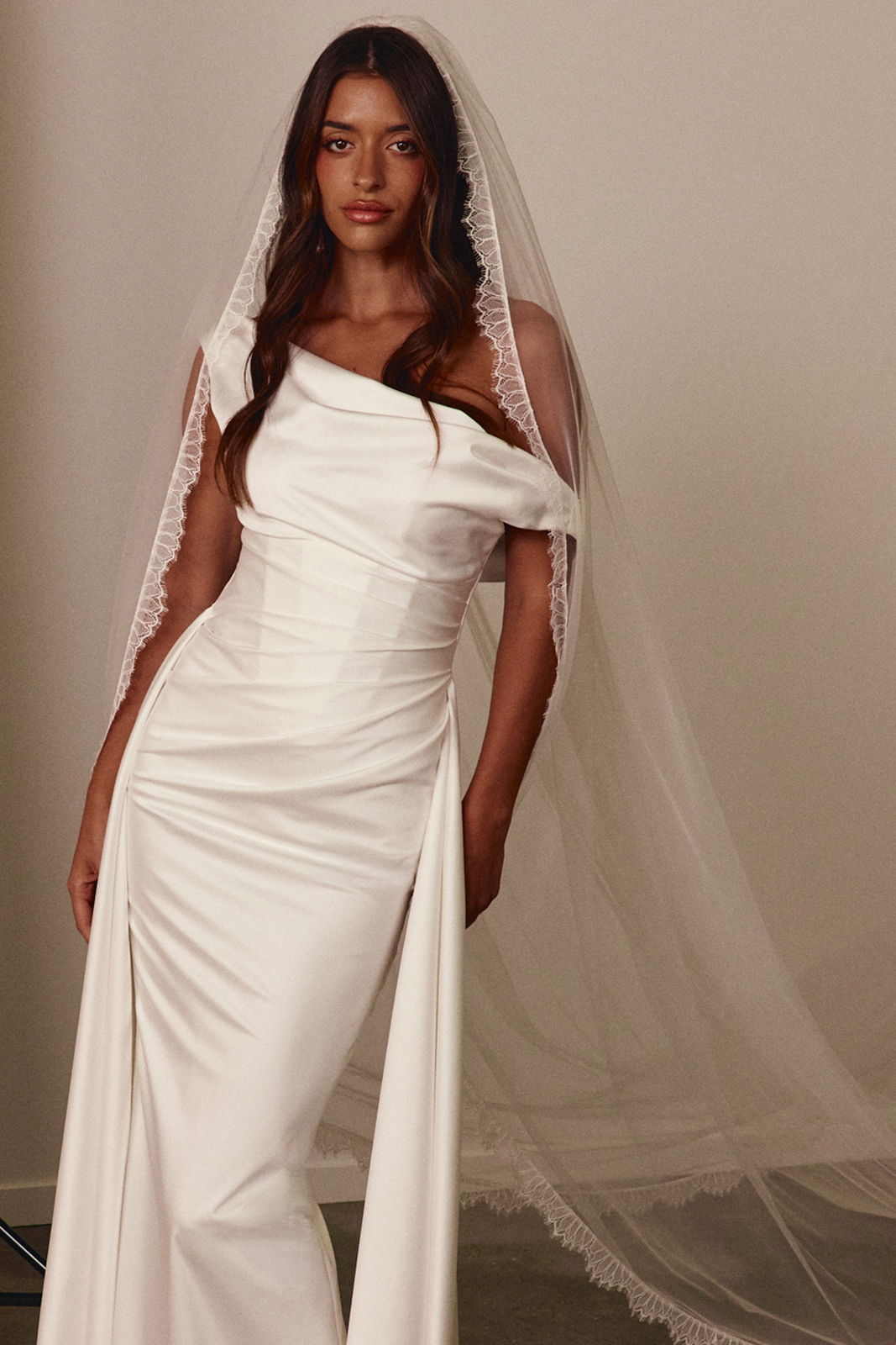 A woman in a white wedding dress and veil poses elegantly.