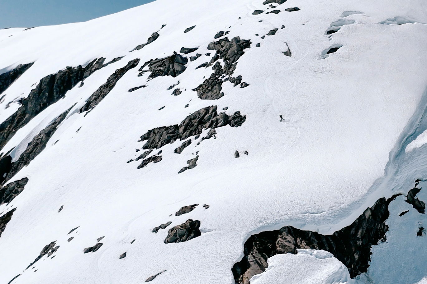 Snow-covered mountain slope with rocky outcrops and clear blue sky.