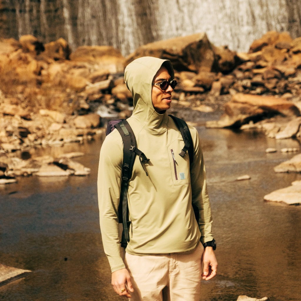 Person in outdoor gear standing near a waterfall and rocky terrain.