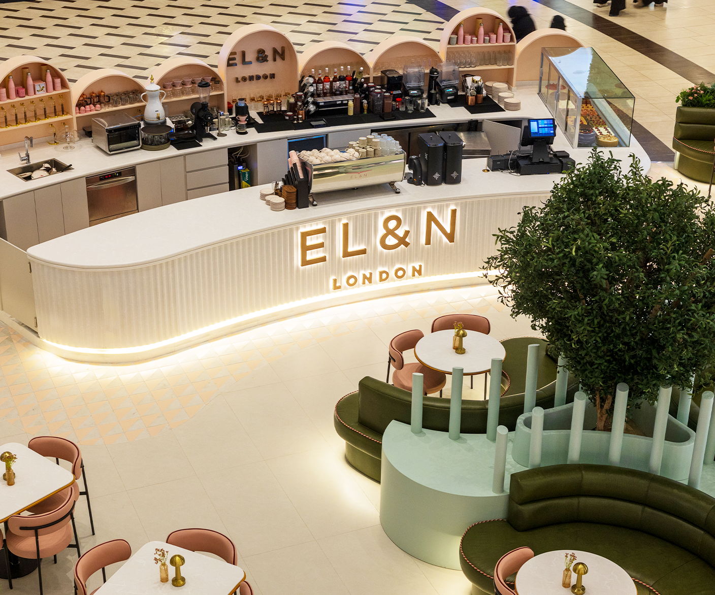 A modern café interior with a counter, tables, and greenery.