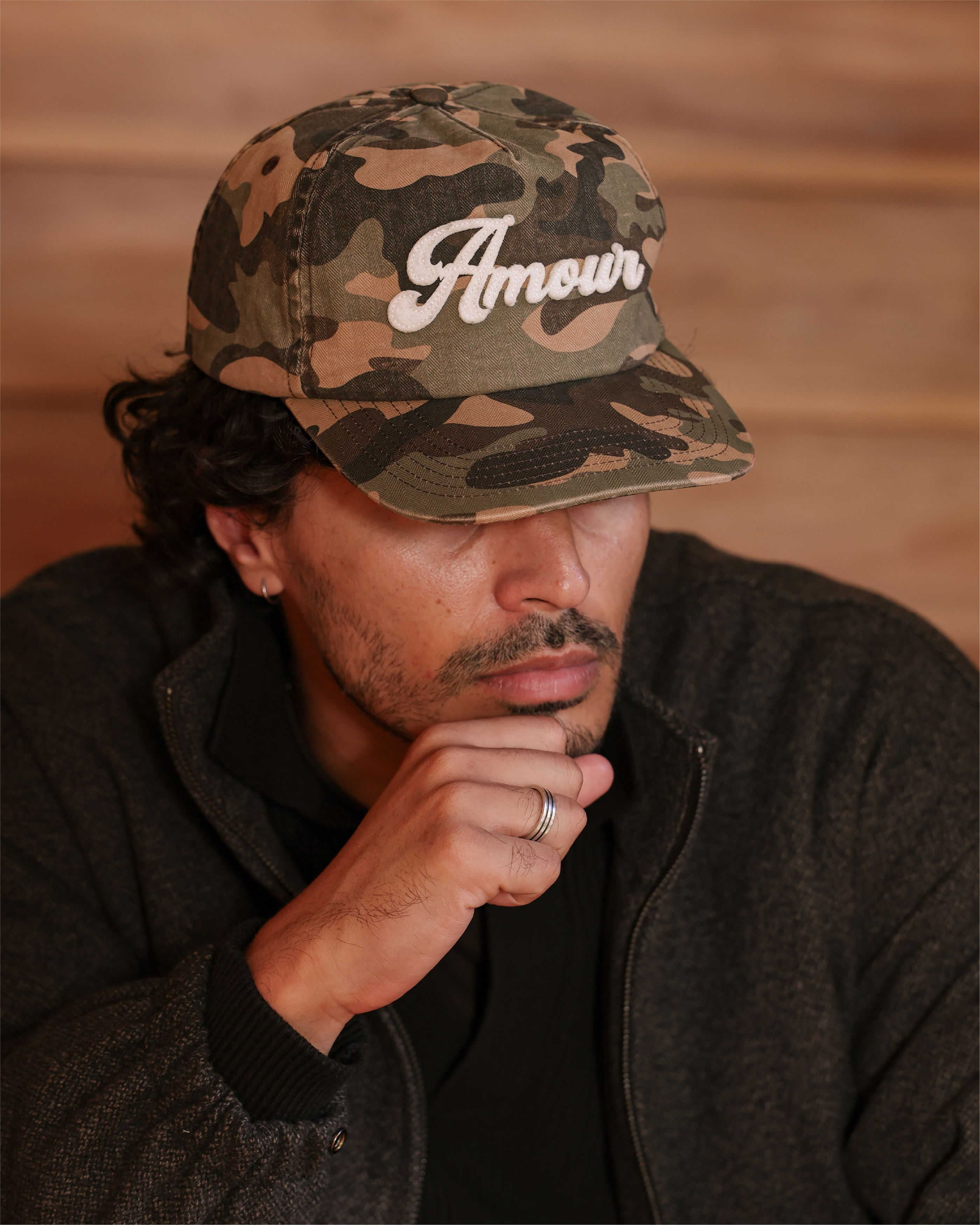 A man in a camouflage cap resting his chin on his hand.