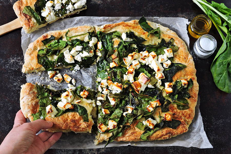 artisanal flatbread pizza with spinach and white cheese, with a hand holding a slice