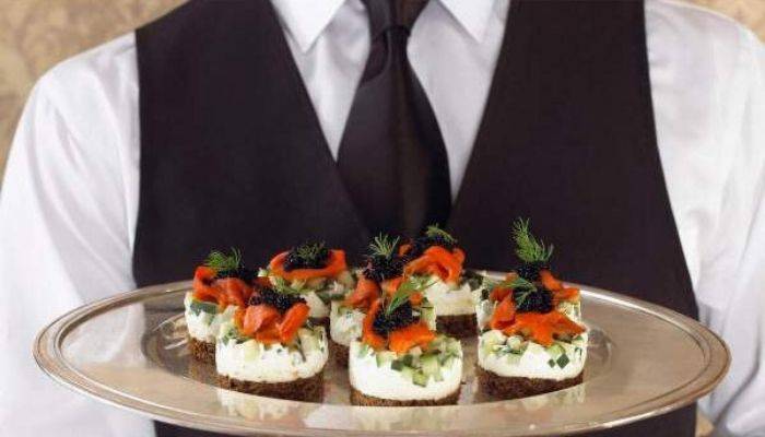 Caterer wearing black tie and vest holding food