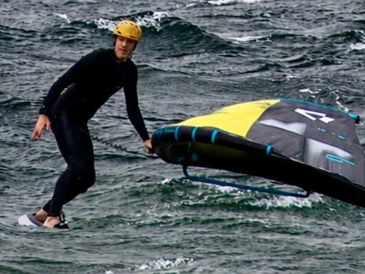 Person surfing on water with a kite-like sail.