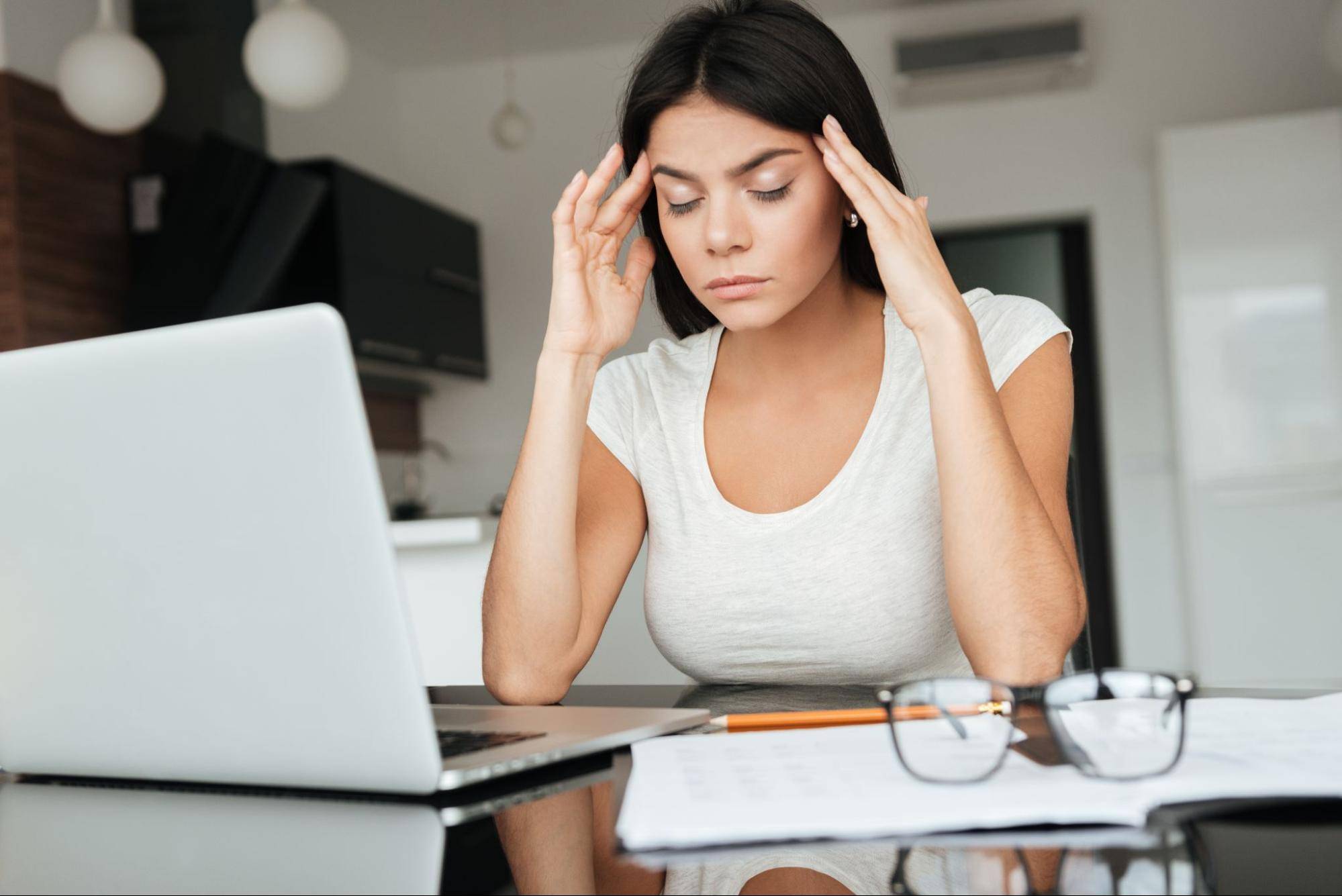 woman at desk with migraine touching her temples