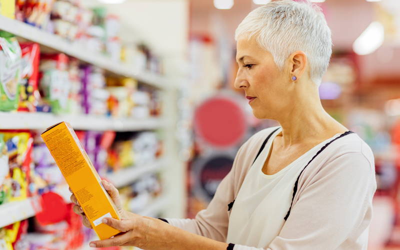 Žena čte složení na obalu výrobku v supermarketu. Pro lidi s potravinovou alergií je to součást každodenního života.