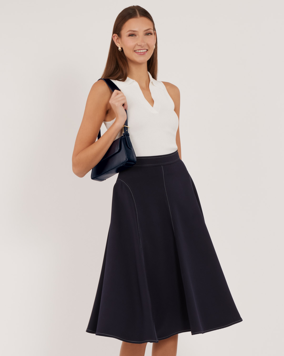 Smiling woman in a white top and navy skirt, holding a bag.