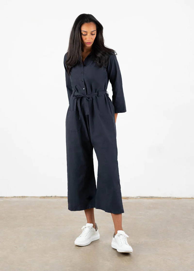 A model wearing a 3/4 length dark blue jumpsuit with white trainers