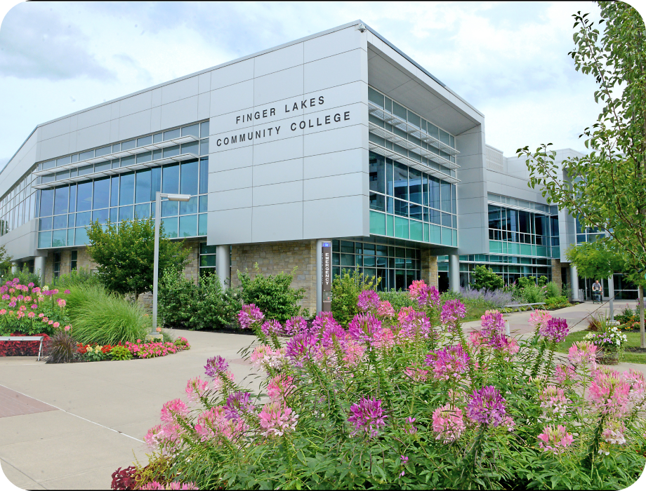 Modern college building surrounded by colorful flowers and greenery.