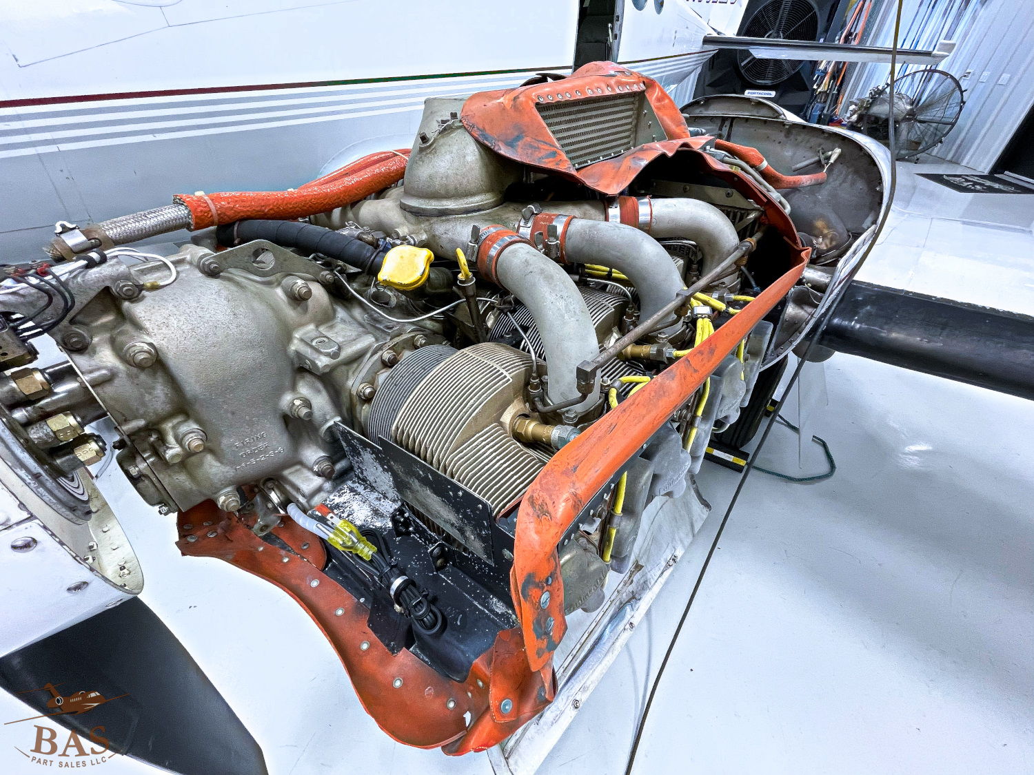 Aircraft engine with exposed components and orange detailing in a hangar.