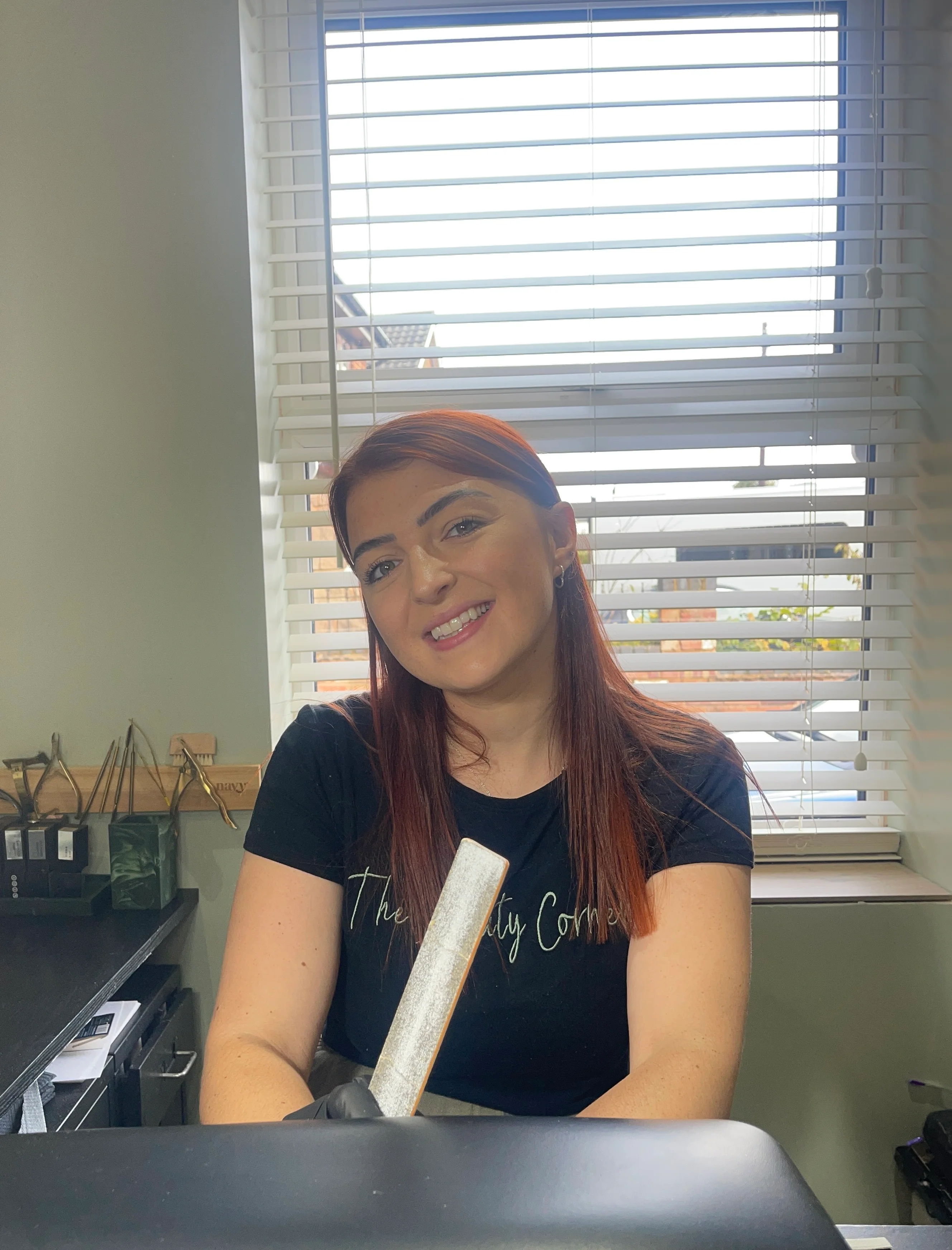 Smiling woman with red hair sitting at a desk by a window.