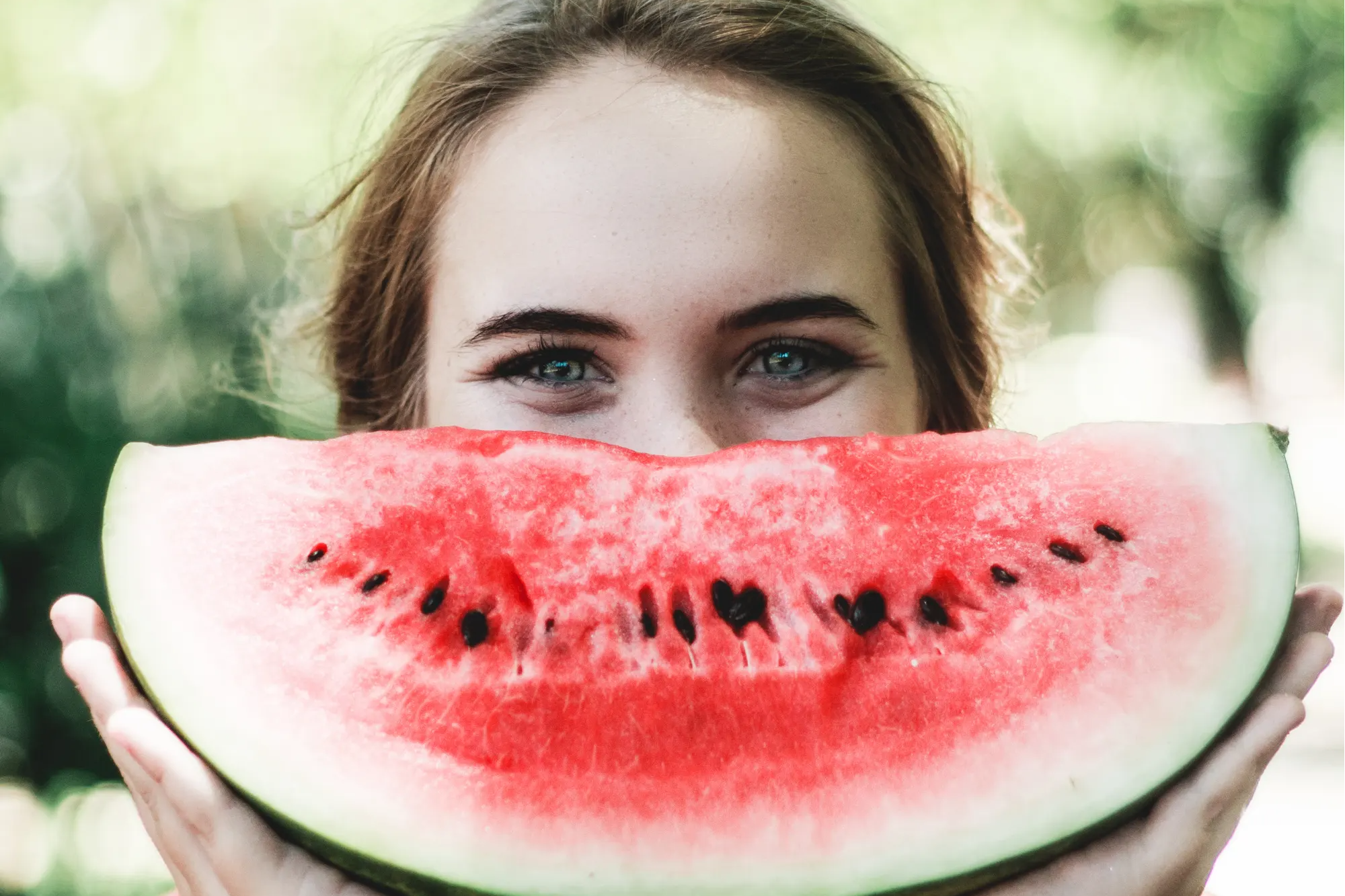woman holding watermelon over mouth as a smile