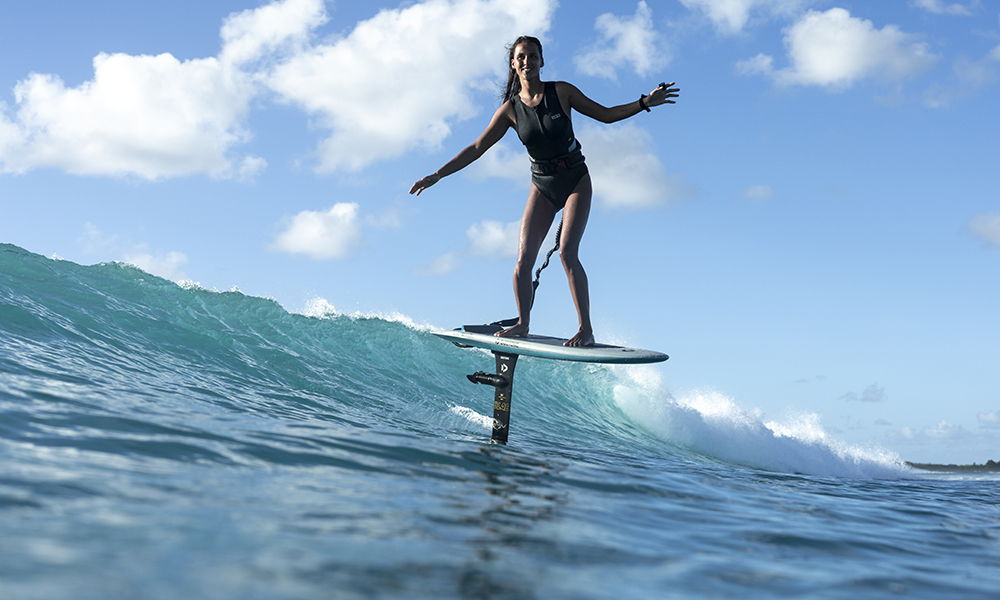 Surfer riding a hydrofoil above ocean waves under a blue sky.