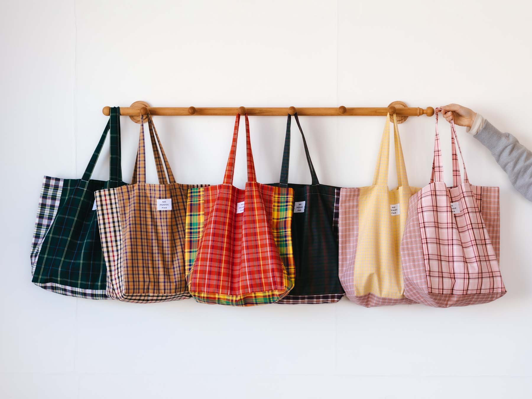 A row of colorful tote bags hanging on a wooden rack.