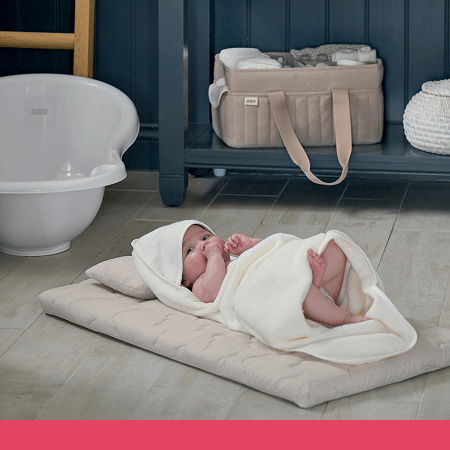 A baby wrapped in a blanket lying on a mat near a bath.