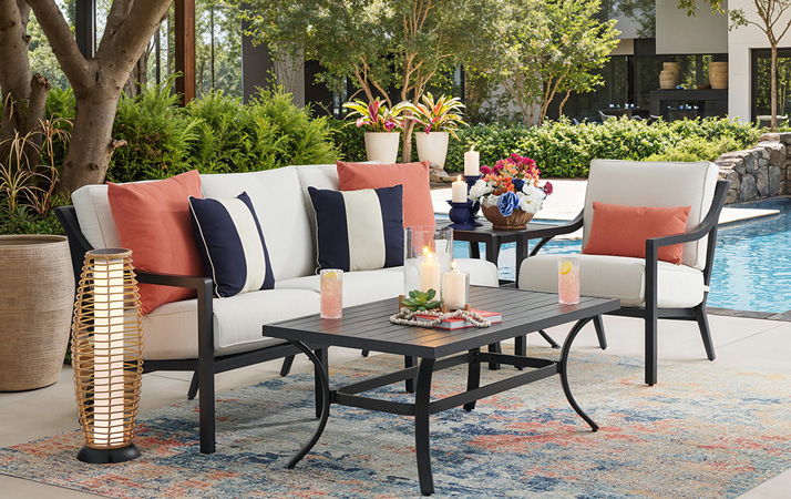 Outdoor seating area with cushions, table, and pool in the background.