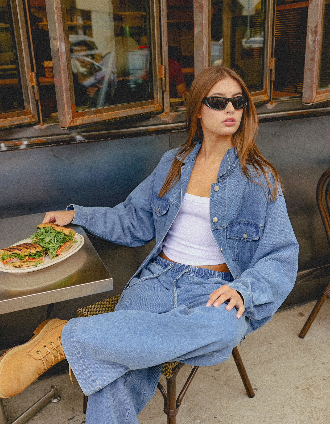 Young woman in denim outfit sitting at a café table with food.