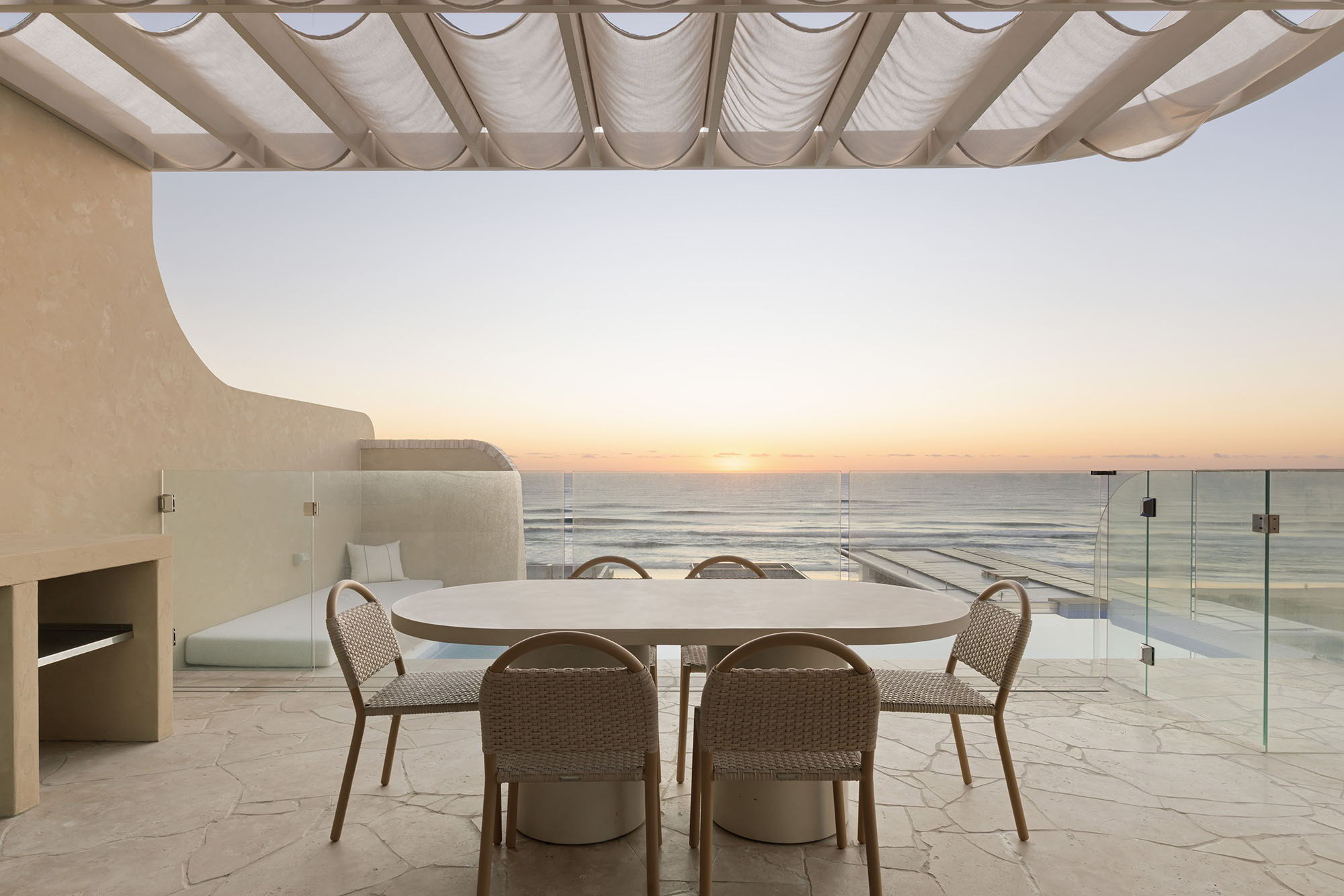 Table and chairs on a terrace overlooking the ocean at sunset.