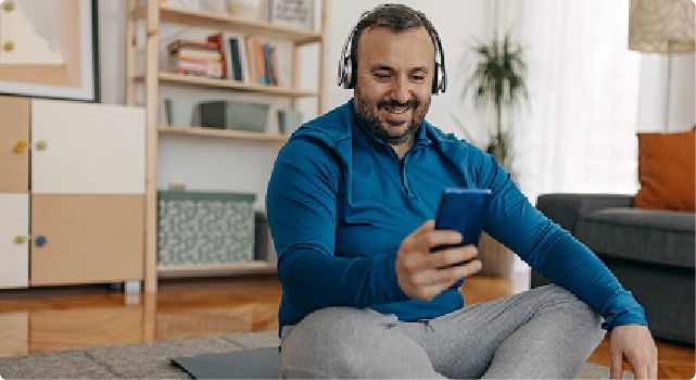 Man sitting on the floor, wearing headphones, looking at his smartphone.