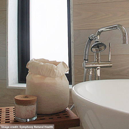 bathroom with white tub, stainless hardware, wooden table with bath salts on it, window in background