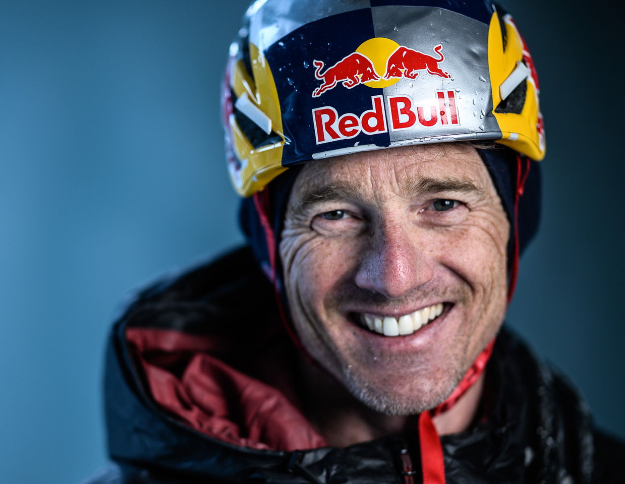 Will Gadd smiling while wearing a helmet with Red Bull logo, against a blue background.