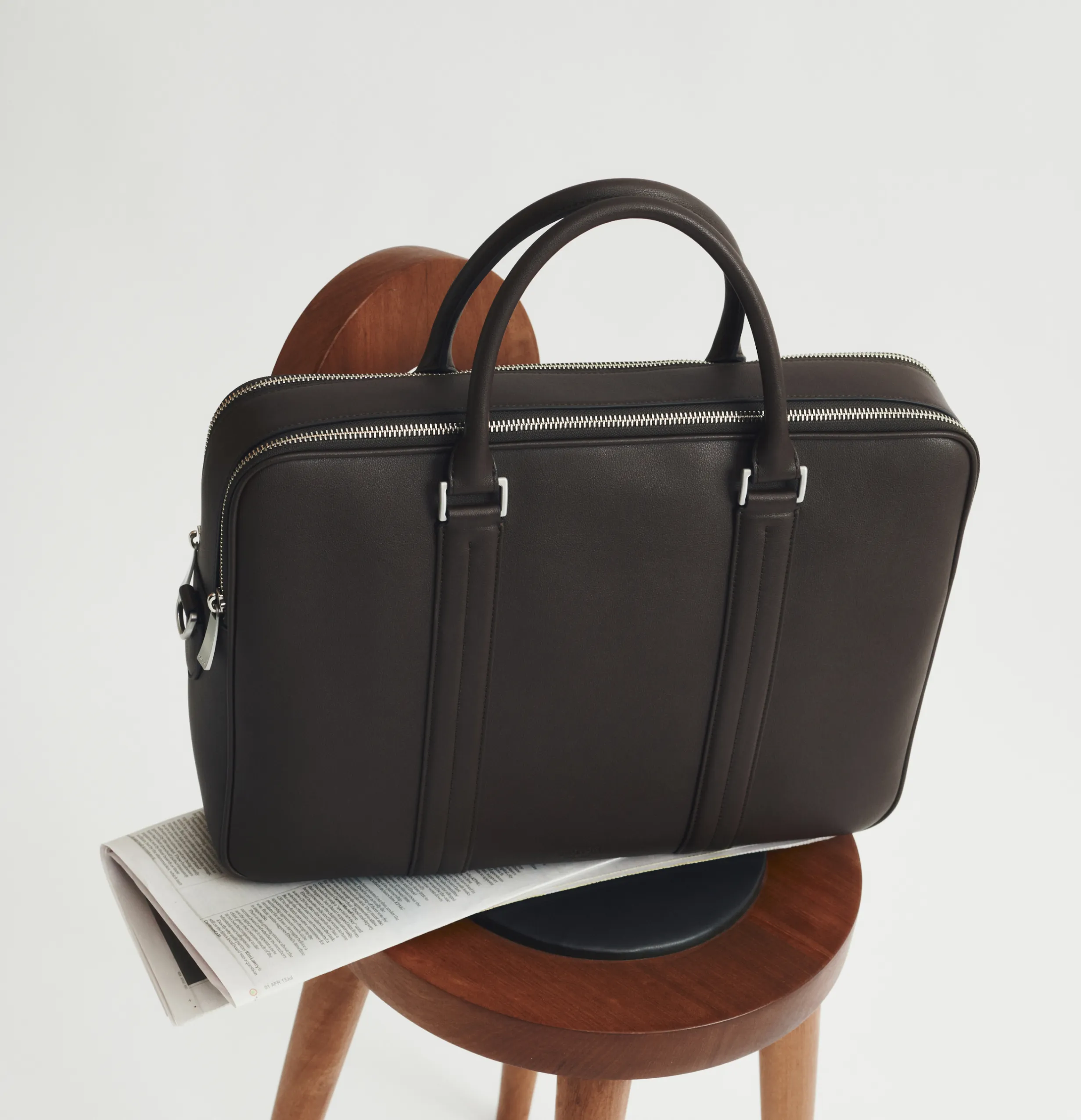 A dark brown briefcase on a wooden chair, resting on a newspaper.