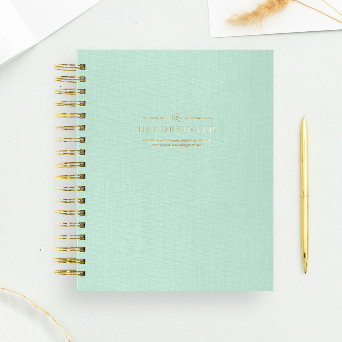 2027 day designer planner featuring sage green cover, gold binding and pen, light green background