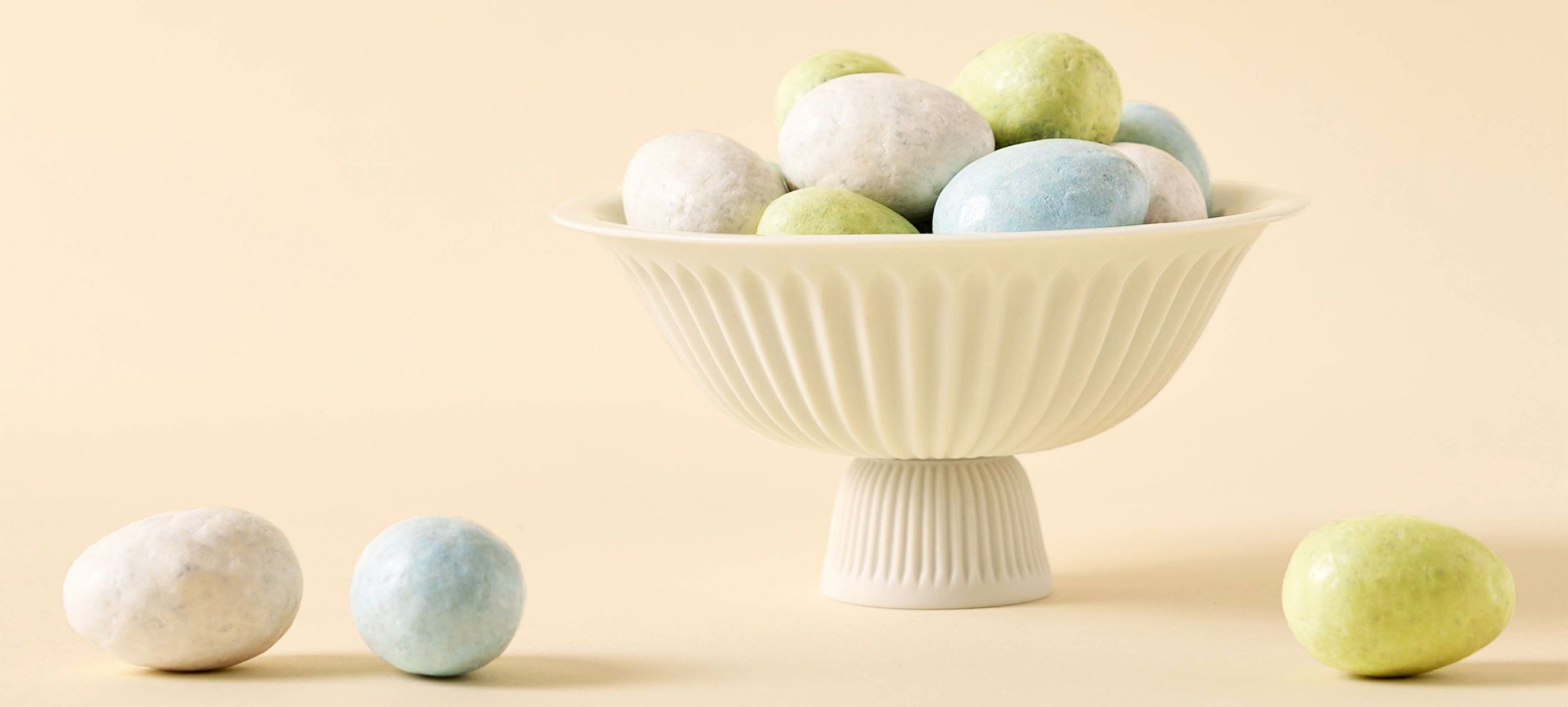 A white bowl filled with colorful decorative eggs on a light background.